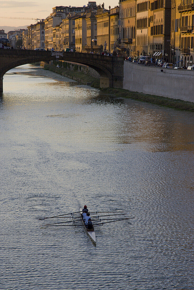 Rowers row toward the Ponte Vecchio at sunset, Florence. Tuscany, Italy