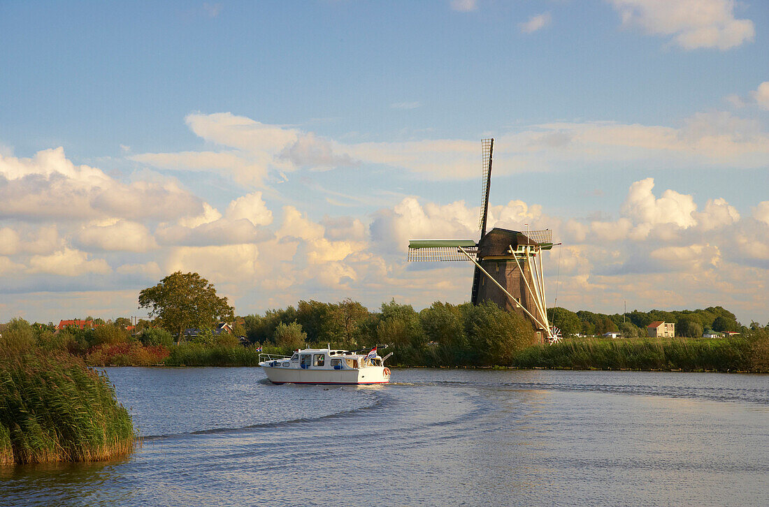 Ein Motorboot auf dem Fluss Vecht fährt an einer Windmühle vorbei, Holland, Europa