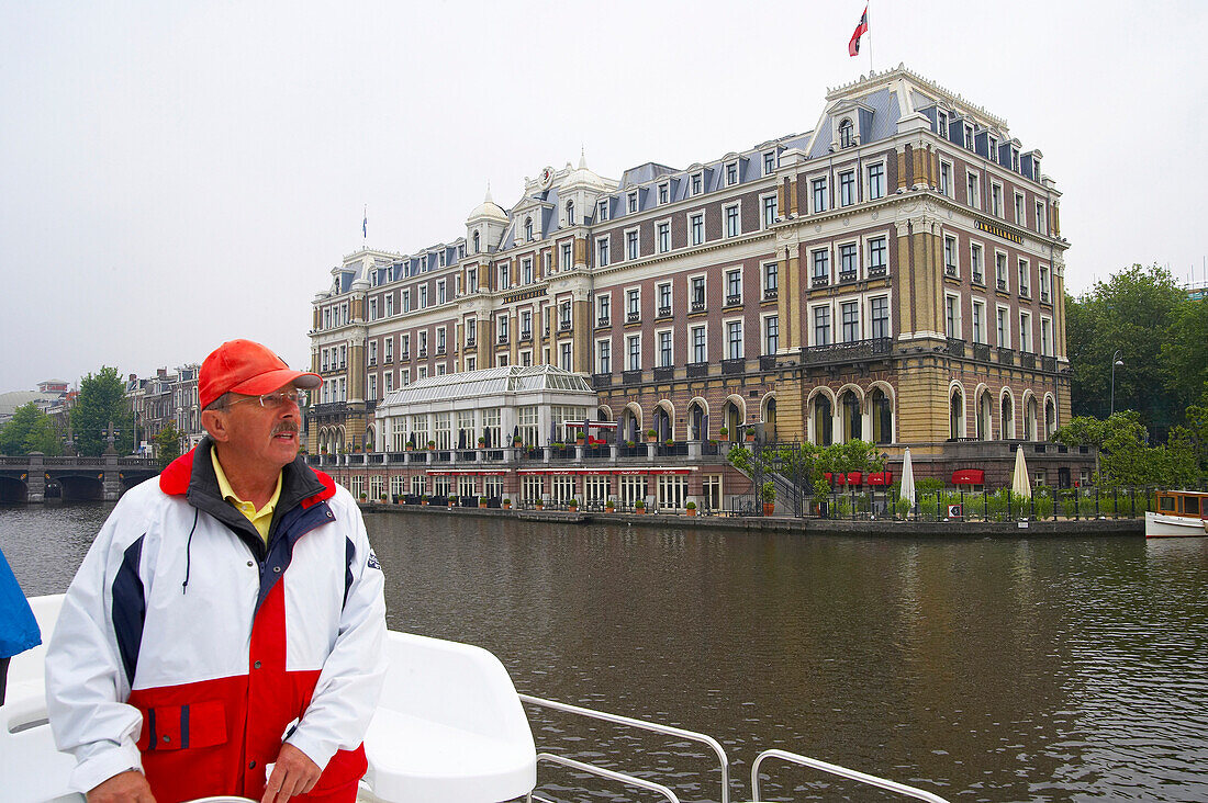 A man on a boat on the river Amstel driving past a hotel, Amsterdam, Netherlands, Europe