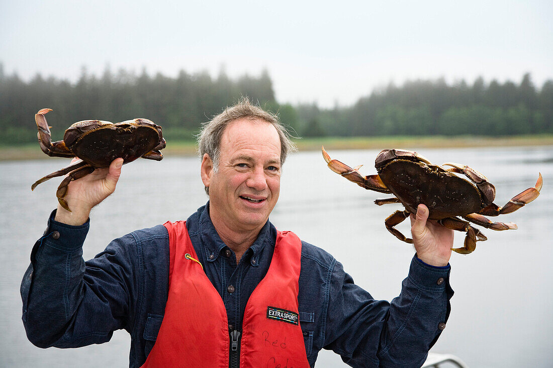 Mature man showing two crabs, Inside Passage, Southeast Alaska, USA