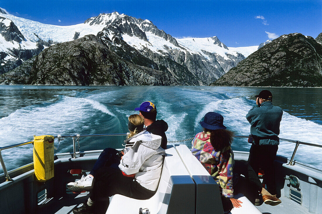 People sitting in the stern of an excursion boat, view at snow covered mountains, Inside Passage, Southeast Alaska, USA