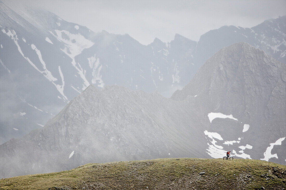Mountainbiker fährt vor einem vernebeltem Alpenpanorama, Ischgl, Tirol, Österreich