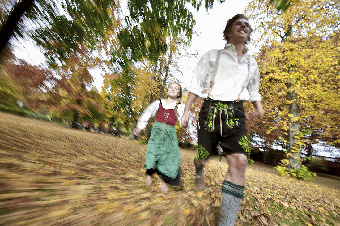 Man and a girl wearing traditional costumes running through a park, Kaufbeuren, Bavaria, Germany