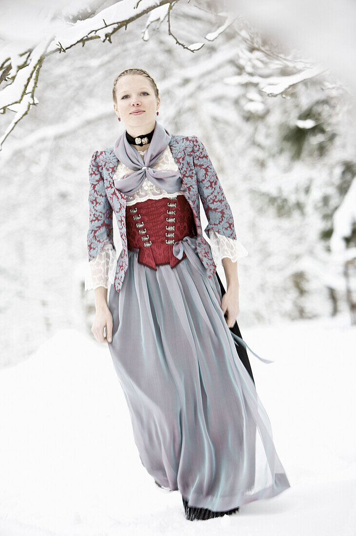 Young woman wearing a Dirndl standing in snowy scenery, Irsee, Bavaria, Germany