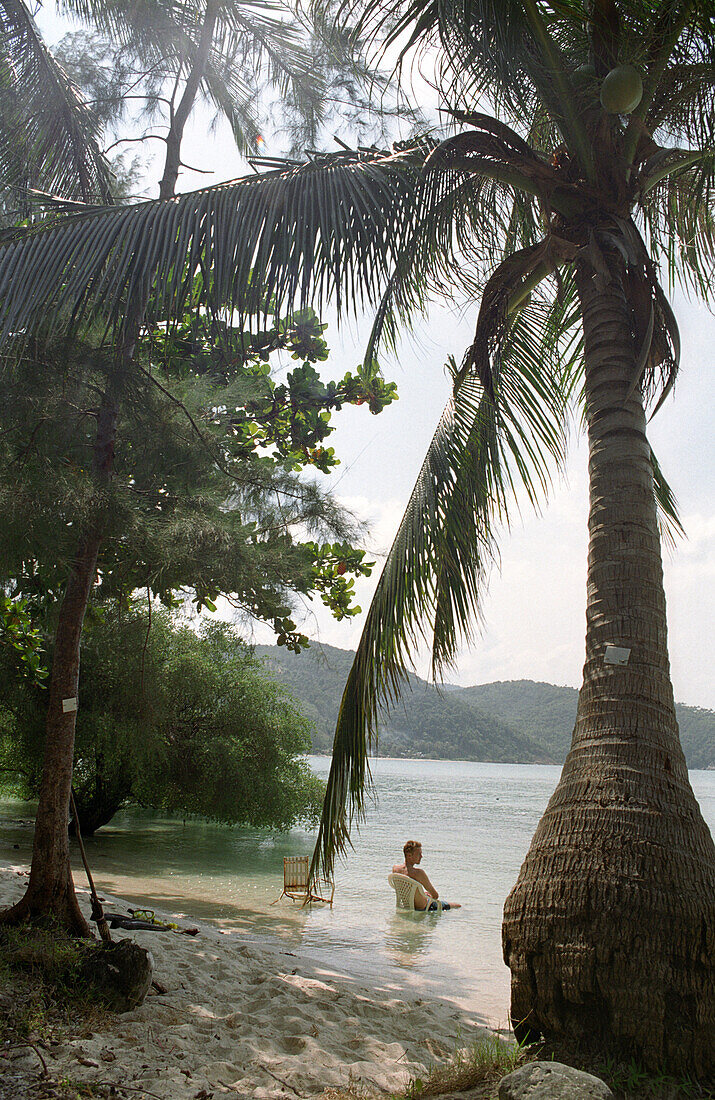 Man sitting at beach in water, Mae Hat Bay, Ko Pha Ngan, Thailand