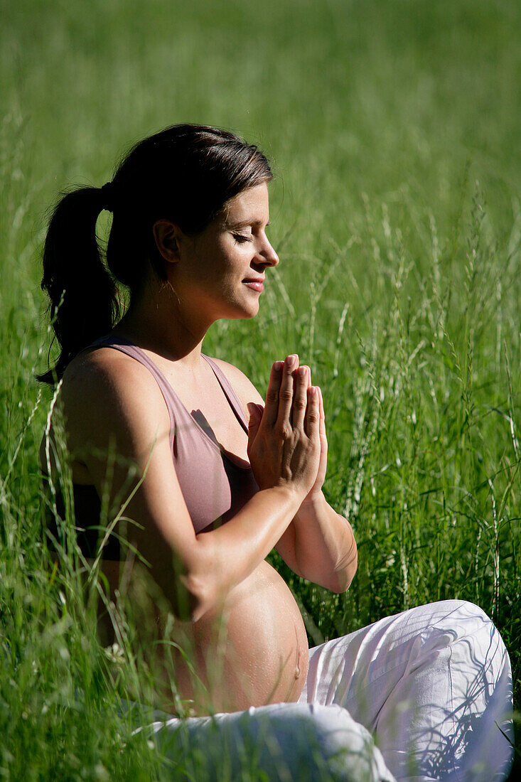Schwangere Frau meditiert in einer Wiese