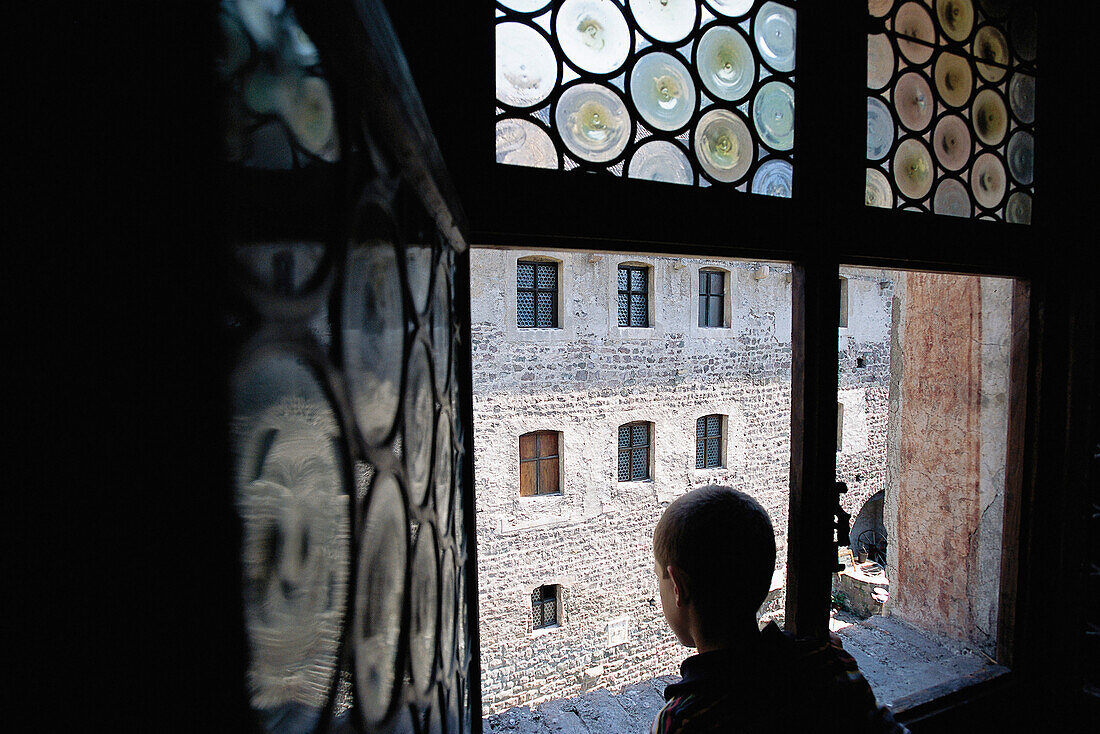 Ein Junge schaut aus einem Fenster von Schloss Runkelstein in den Innenhof, Südtirol, Italien, Europa