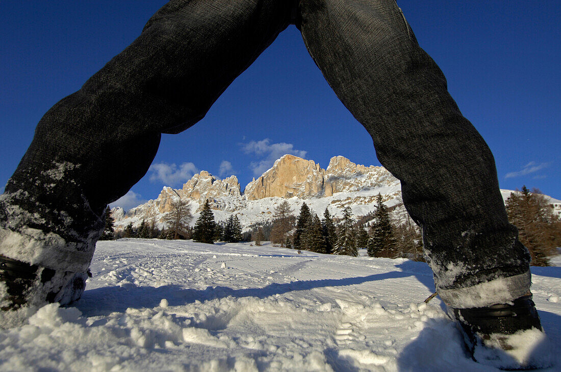 Blick durch die Beine eines Kindes auf Winterlandschaft unter blauem Himmel, Dolomiten, Südtirol, Italien, Europa