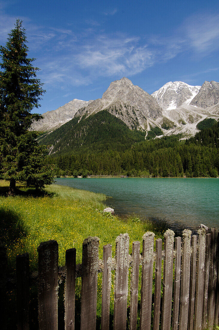 Holzzaun vor dem Antholzersee in idyllischer Berglandschaft im Sonnenlicht, Pustertal, Südtirol, Italien, Europa