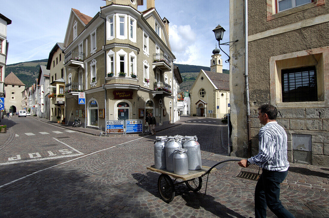 Ein Mann schiebt einen Handwagen mit Milchkannen über eine Strasse der Altstadt, Glurns, Vinschgau, Südtirol, Italien, Europa
