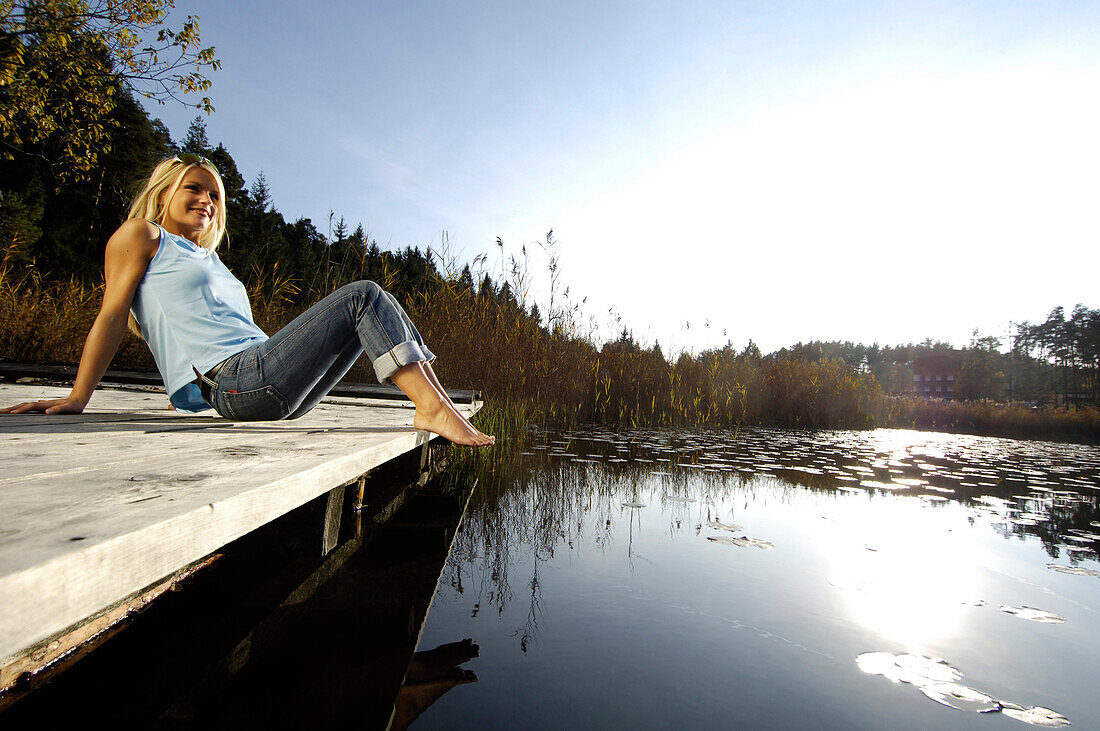 Young woman sunbathing on a jetty at a mountain lake, Völs am Schlern, South Tyrol, Italy, Europe