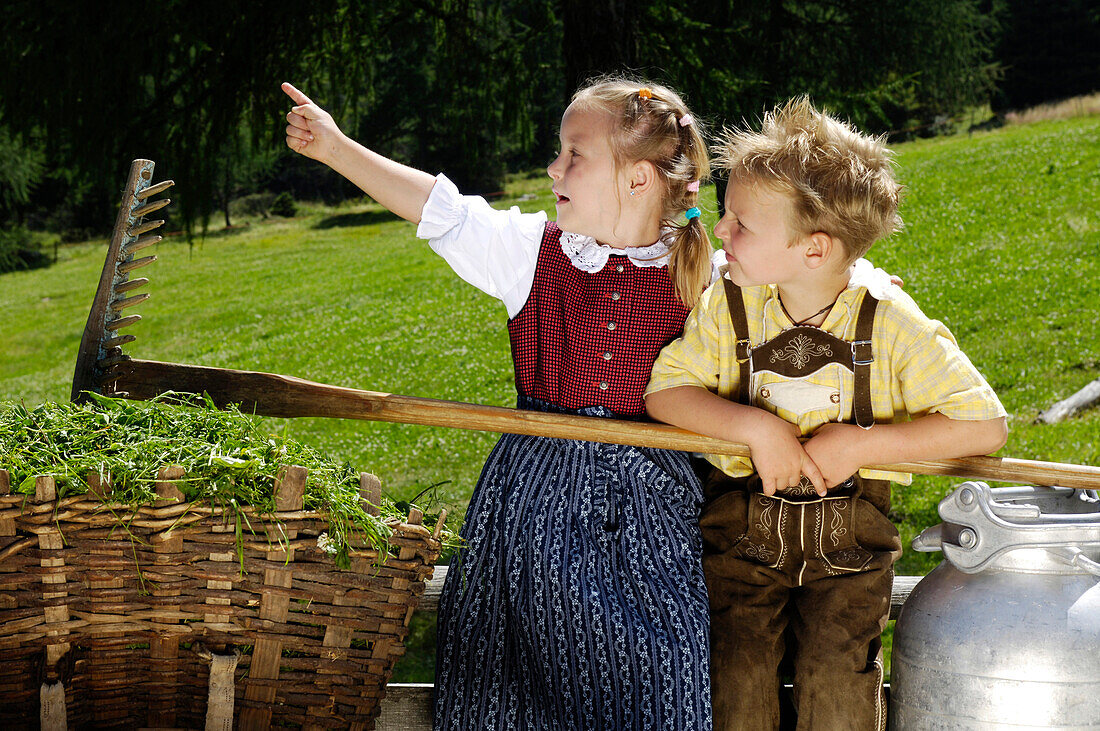 Girl and boy wearing traditional clothes with basket and milk can, Alpine meadow, Agriculture, South Tyrol, Italy