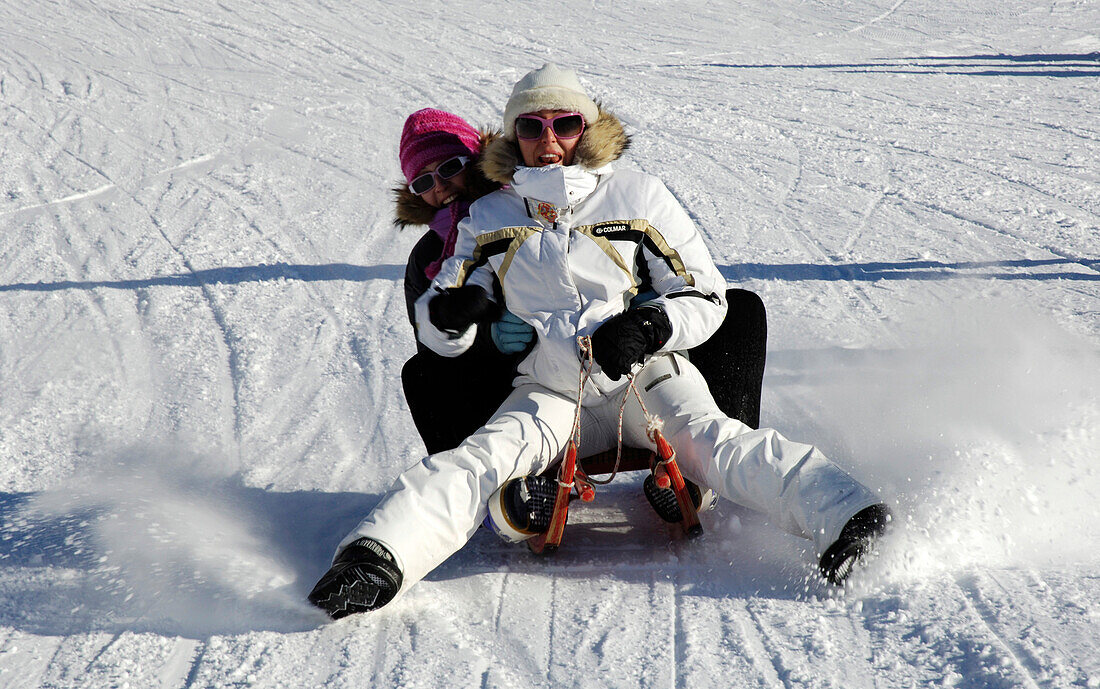 Two women on a sledge, sledging down a slope, Fun in the snow, South Tyrol, Italy