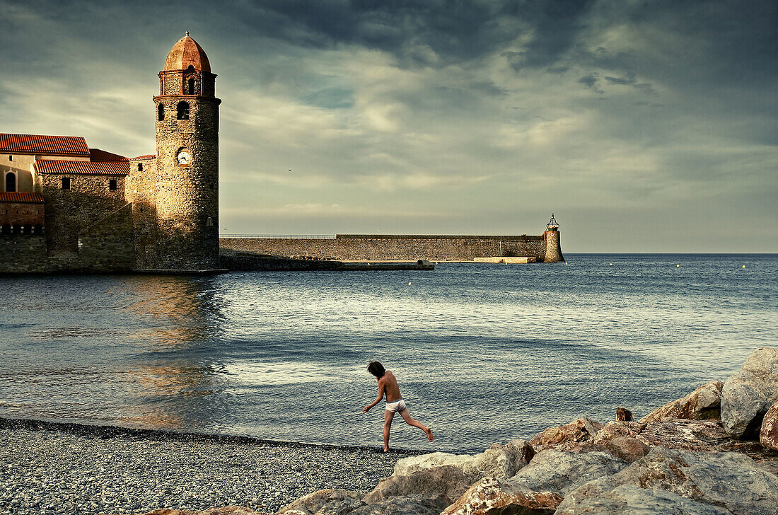 Boy on the beach and Notre-Dame des Anges church in background, Collioure. Roussillon-Languedoc, Pyrenees Orientales, France