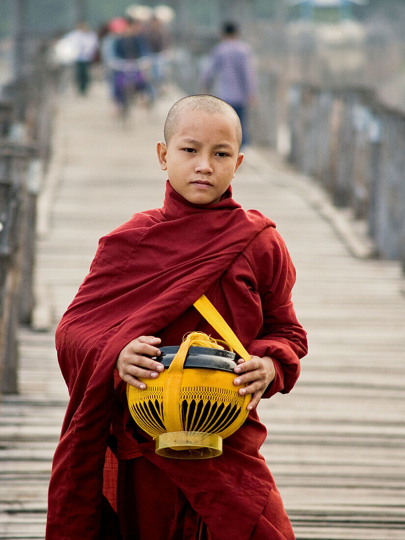 Portrait of a young monk with his alms bowl on the U Bein teak bridge in Myanmar