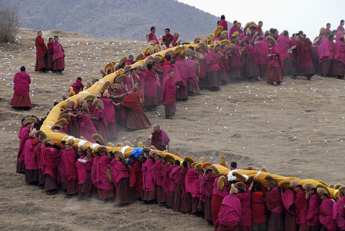 a long line of monks is carrieng a huge Tanka up a maountain in Labrang monastery in Qinghai provice China