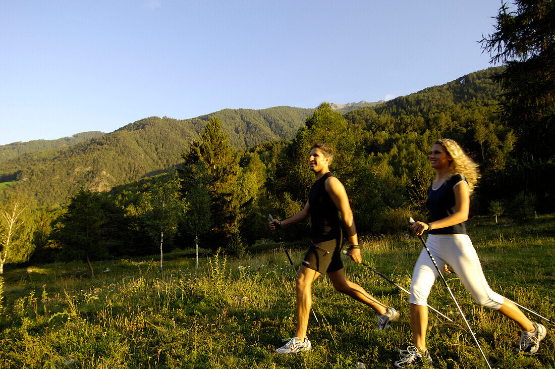 Junges Paar beim Nordic Walking im Sonnenlicht, Vinschgau, Südtirol, Italien, Europa