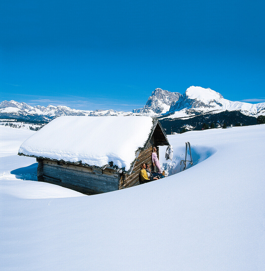 Menschen nehmen Sonnenbad an verschneiter Almhütte, Seiser Alm, Eisacktal, Südtirol, Italien, Europa