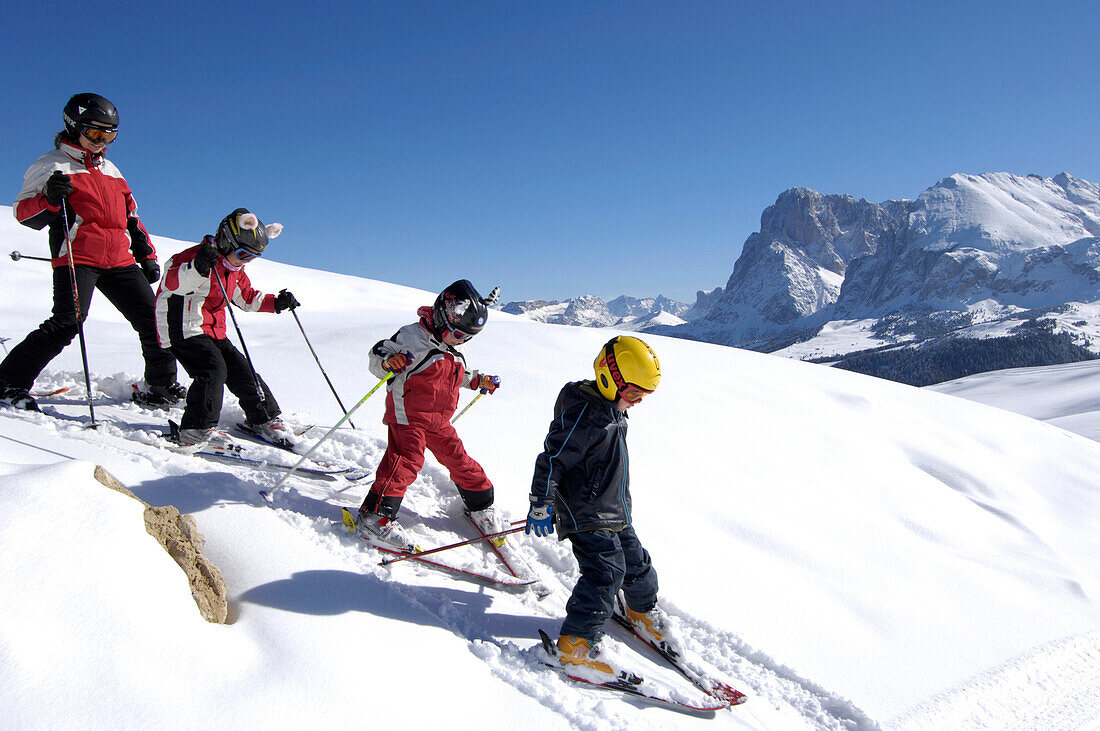 Eine Gruppe Kinder fährt Ski unter blauem Himmel, Dolomiten, Südtirol, Italien, Europa