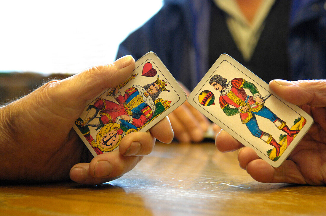 Hands holding playing cards above a table, seniors playing cards at a tavern, South Tyrol, Italy, Europe