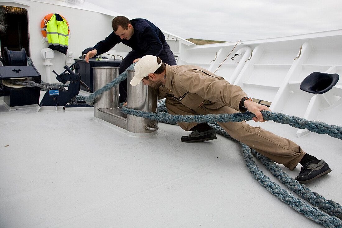 Two men on board the yacht Hanse Explorer pulling a mooring rope, journey around Shetland Islands, Scotland, Great Britain
