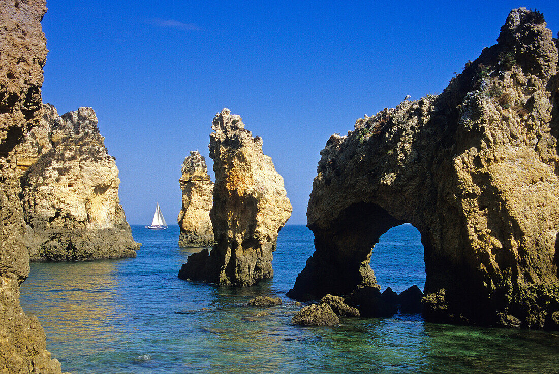 A sailing boat off the rocky coast under blue sky, Ponta da Piedade, Algarve, Portugal, Europe