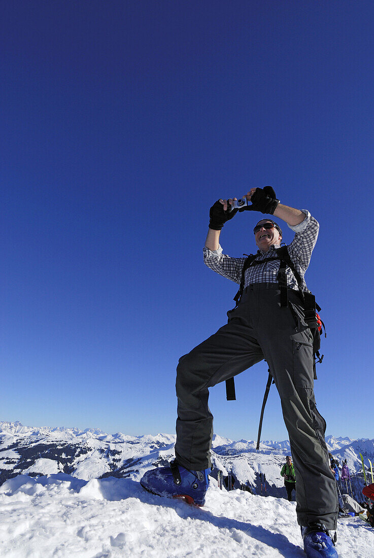 Backcountry skier taking summit shot with digital camera, Brechhorn, Kitzbuehel range, Tyrol, Austria