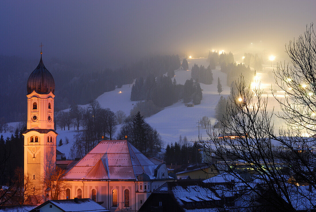 Blick über Pfarrkirche St. Andreas auf beleuchtete Skipiste, Nesselwang, Bayern, Deutschland