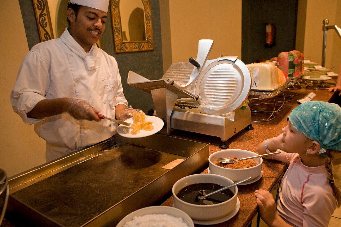 Koch bei Zubereitung eines Pfannkuchens für ein Kind, Mädchen, 5, am Buffet des Lamaya Resort, Coraya, Marsa Alam, Aegypten