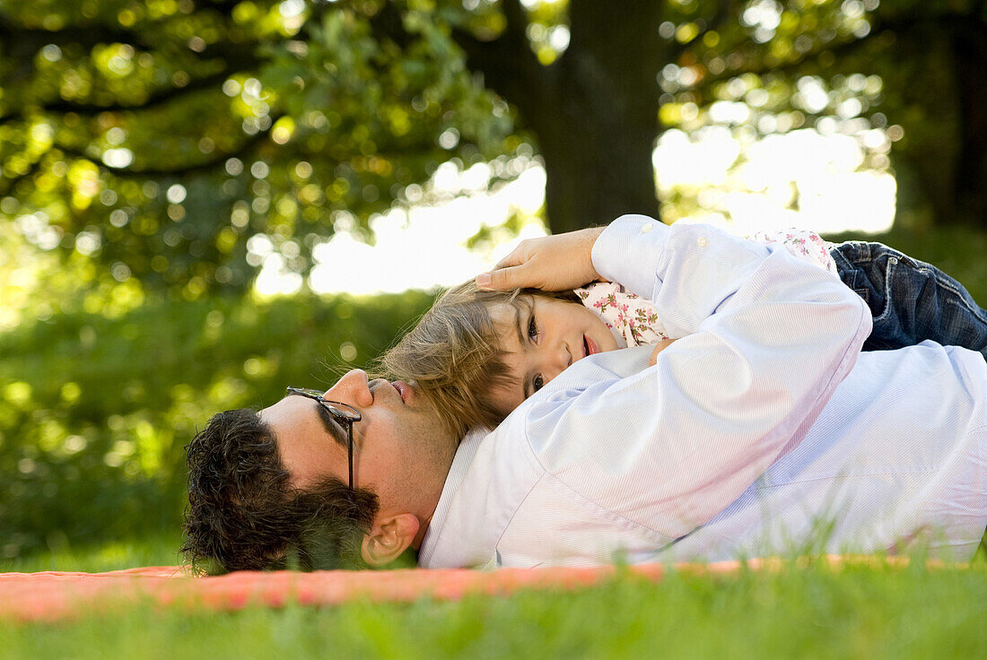 Father and daughter (2-3 years) lying on grass, English Garden, Munich, Bavaria, Germany