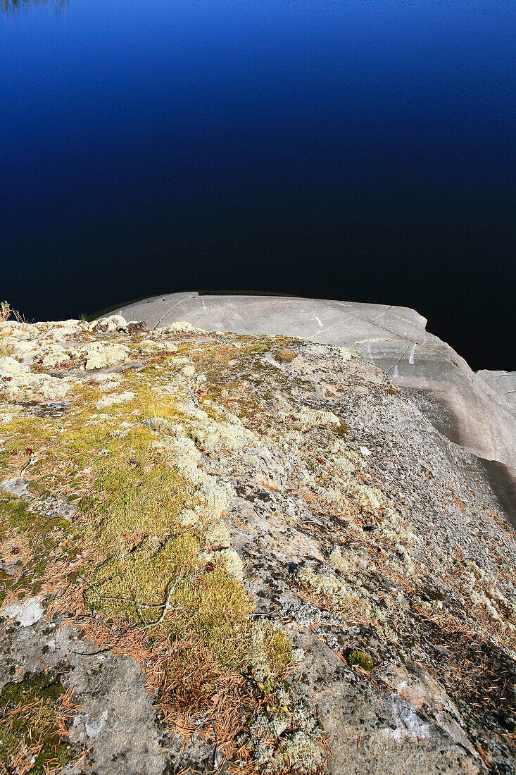 Moosbewachsener Stein am Ufer einer unbewohnten Insel im Sonnenlicht, Saimaa Seenplatte, Finnland, Europa