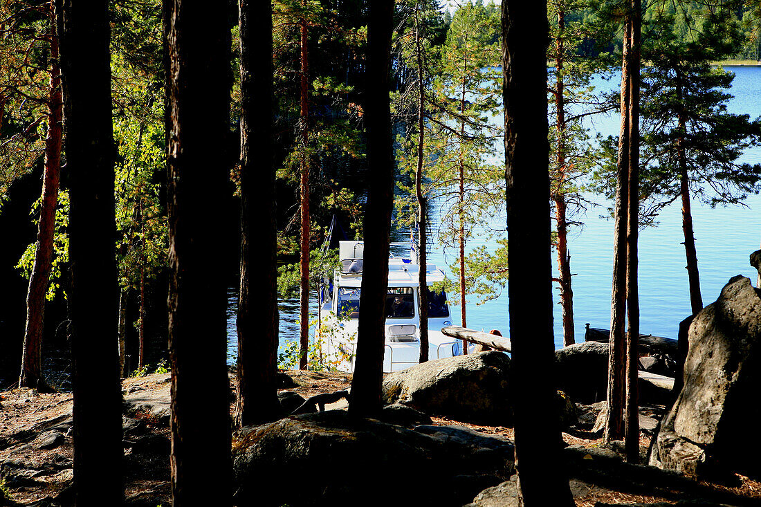 Blick durch Bäume auf eine Jacht am Ufer, Insel Linnansaari, Nationalpark Linnansaari, Saimaa Seenplatte, Finnland, Europa