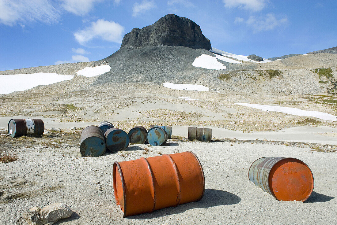Fuel drums abandoned by miners and left to rust and leak into the wilderness watershed of Salal Creek, The Elephant, or sometimes called The Black Molar 2314 m 7592 ft is in the distance Coast Mountains British Columbia