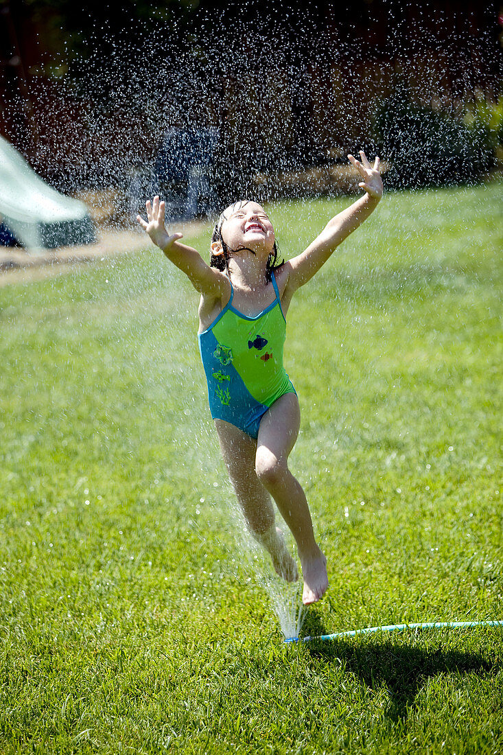 Young girl leaps through yard sprinkler