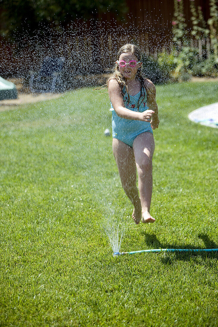 Young girl runs through yard sprinkler