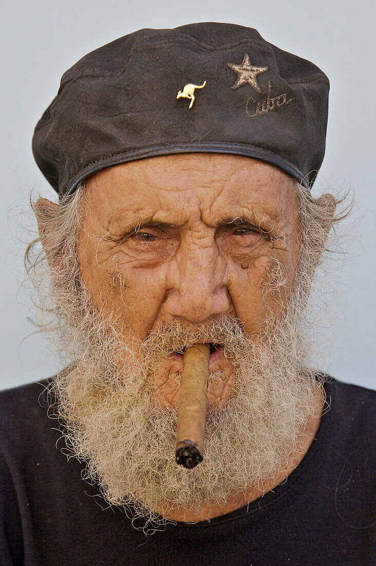 An old Cuban man wearing a beret and smoking a cigar.