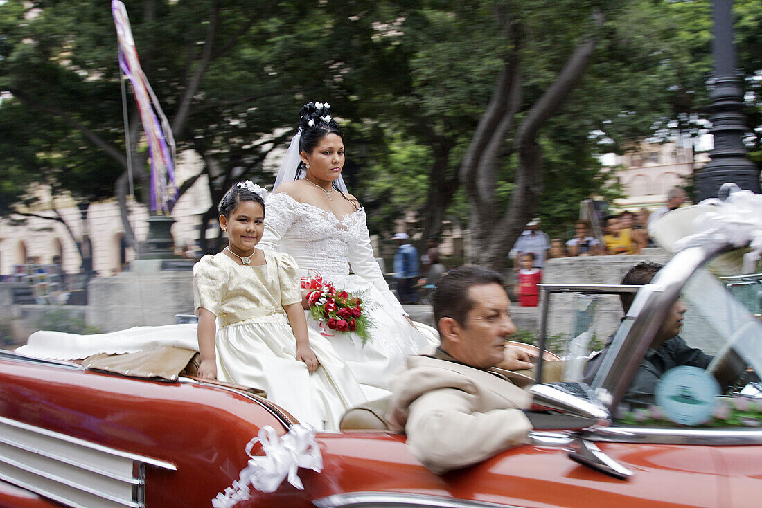 A bride and groom cruising the streets in an open convertible car.