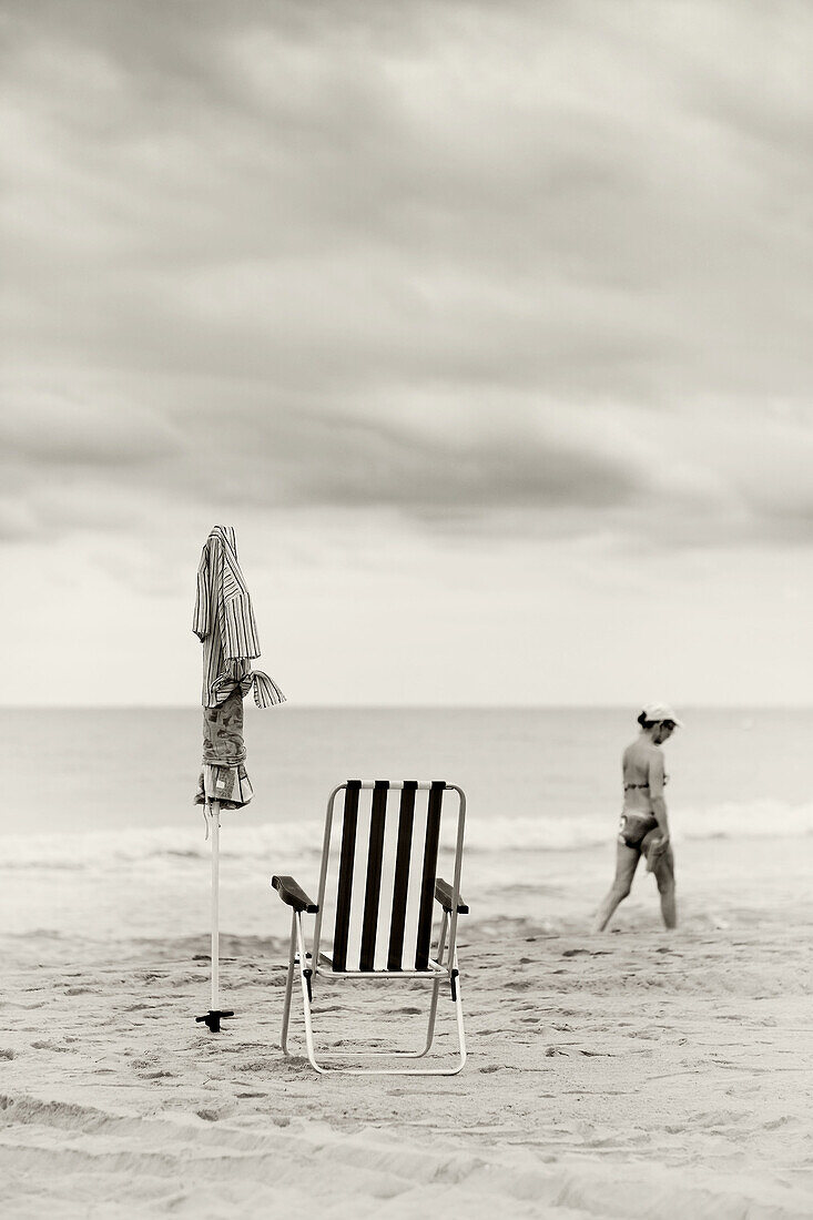 Bañista solitaria paseando por la playa al final del verano. Sombrilla espectadora.