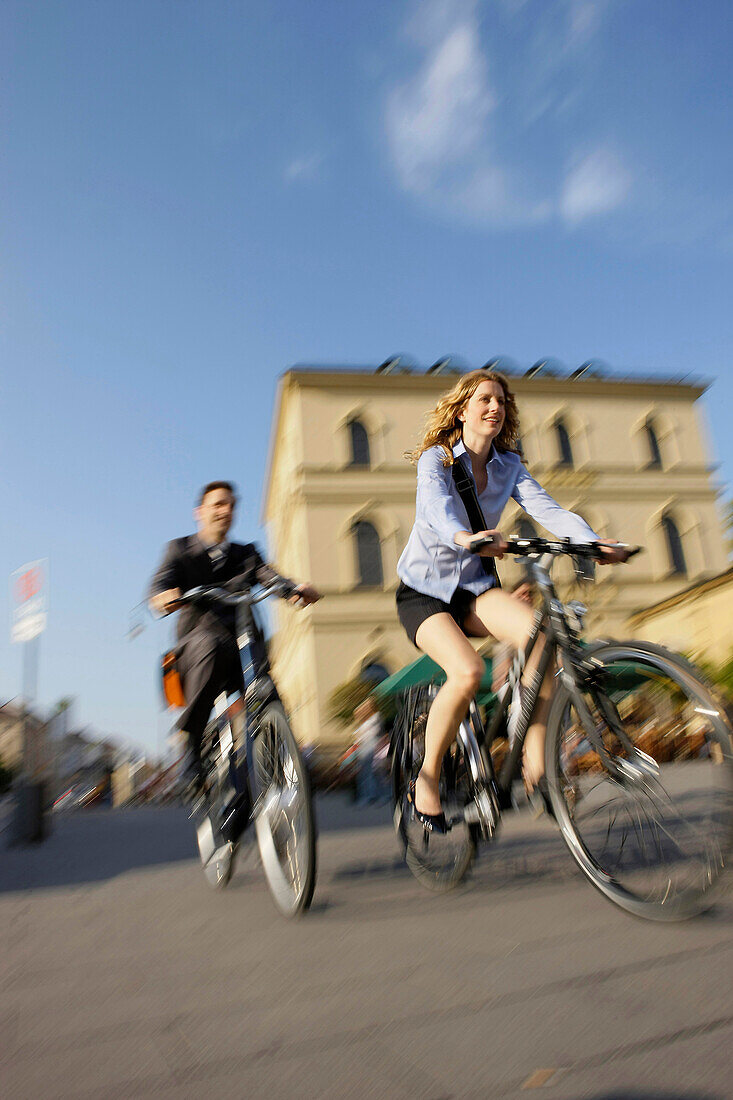 Two businesspeople riding bicycles at Odeonsplatz, Munich, Bavaria, Germany