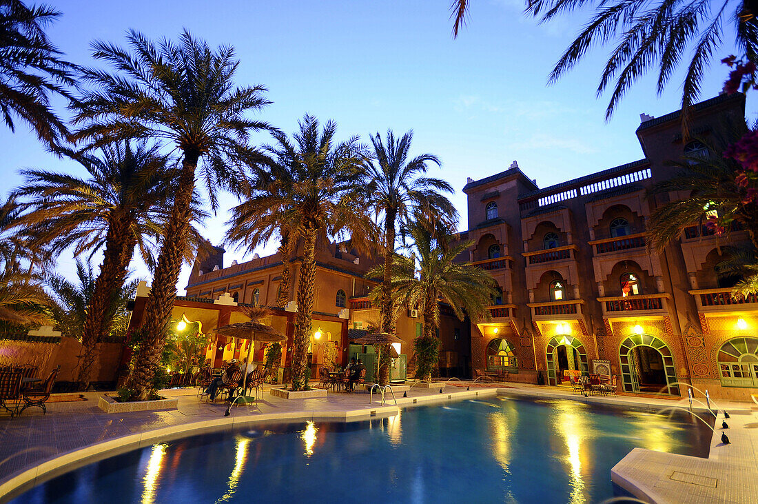Illuminated pool beneath palm trees at Hotel Asmaa in the evening, Zagora, Draa valley, South Morocco, Morocco, Africa
