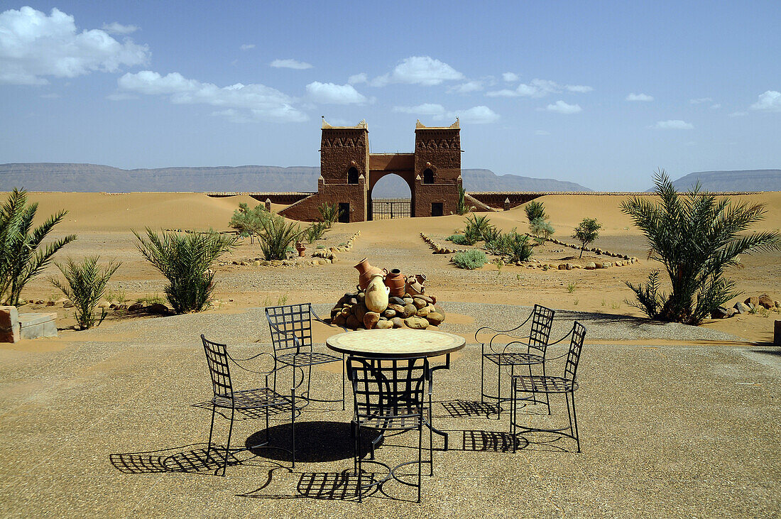Tisch und Stühle auf einer Terrasse im Sonnenlicht, Blick auf ein Tor, Draa-Tal, Süd Marokko, Marokko, Afrika