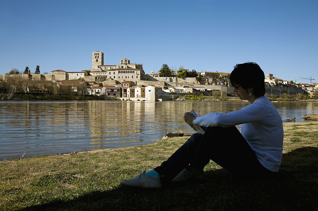 Woman reading by Duero river with Zamora in background. Castilla-Leon, Spain