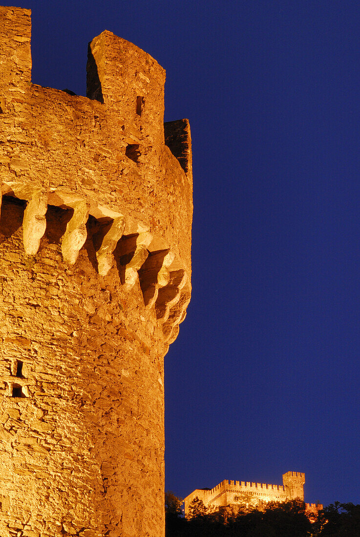 Rundturm der Burg Castello di Montebello, beleuchtet, mit Castello di Sasso Corbaro im Hintergrund in UNESCO Weltkulturerbe Bellinzona, Bellinzona, Tessin, Schweiz