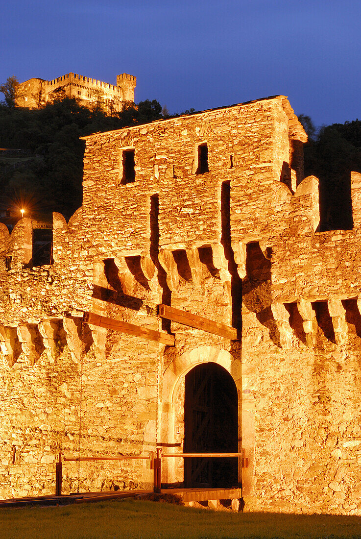 Zugbrücke der Burg Castello di Montebello, beleuchtet, mit Castello di Sasso Corbaro im Hintergrund in UNESCO Weltkulturerbe Bellinzona, Bellinzona, Tessin, Schweiz