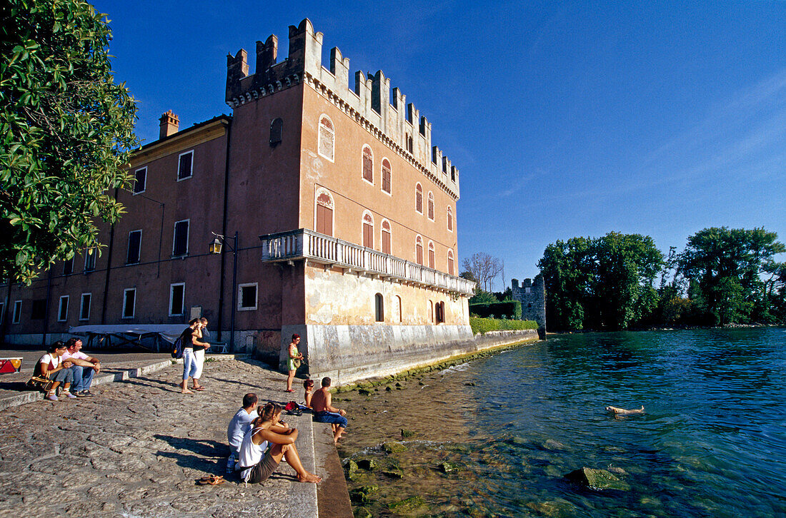 Menschen sitzen am Seeufer vor der Skaligerburg, Lazise, Gardasee, Venetien, Italien, Europa