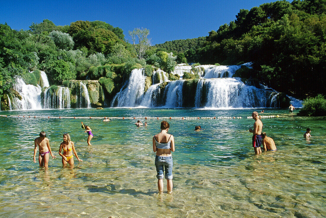 Menschen baden an den Krka Wasserfällen im Sonnenlicht, Krka Nationalpark, Kroatische Adriaküste, Dalmatien, Kroatien, Europa