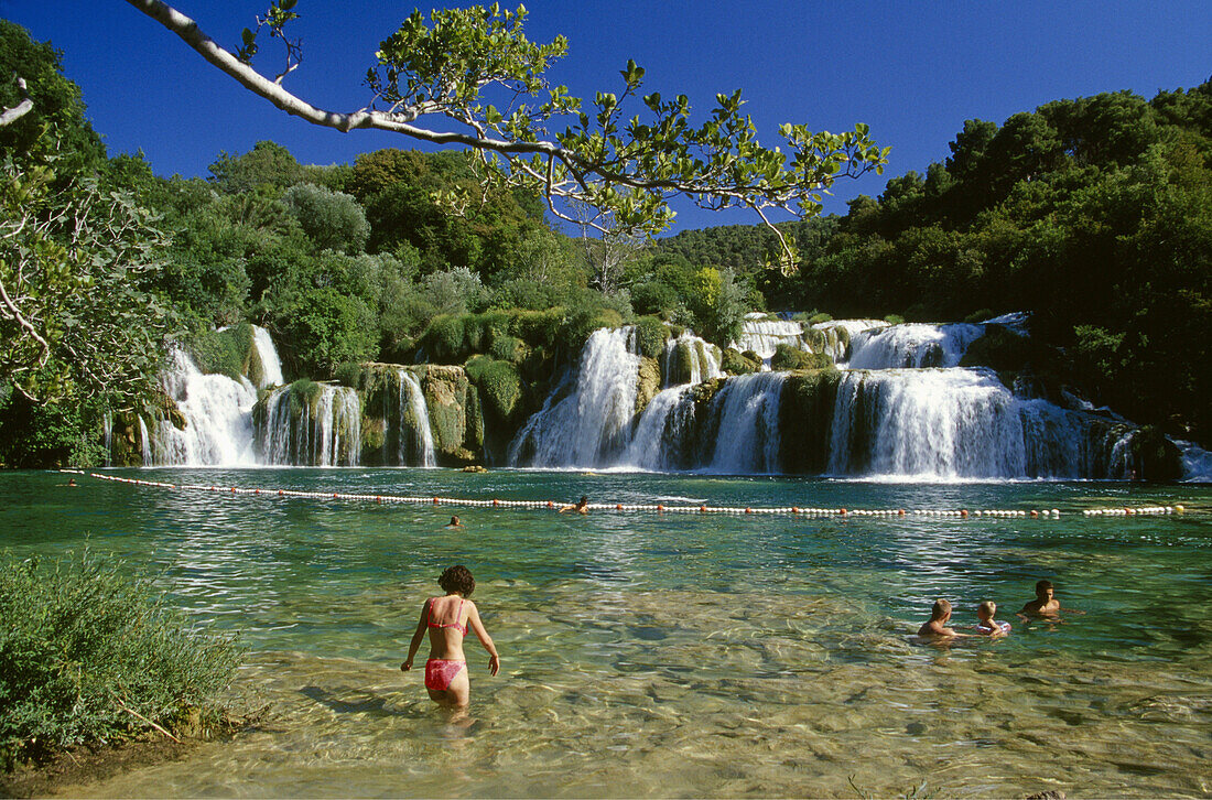 Menschen baden an den Krka Wasserfällen unter blauem Himmel, Krka Nationalpark, Kroatische Adriaküste, Dalmatien, Kroatien, Europa