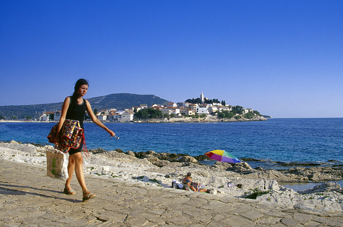 Junge Frau geht über die Strandpromenade von Primosten, Kroatische Adriaküste, Dalmatien, Kroatien, Europa