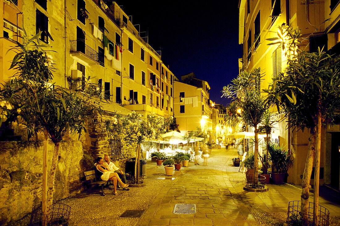 Couple sitting on a bench in front of illuminated restaurants, Vernazza, Cinque Terre, Liguria, Italian Riviera, Italy, Europe