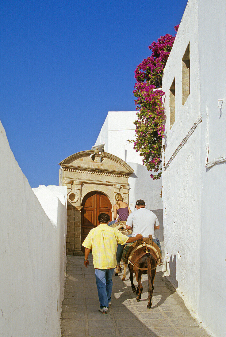 Mann und Frau reiten auf Eseln durch eine Gasse, Lindos, Rhodos, Griechenland, Europa